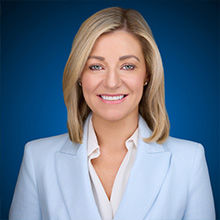 Headshot of Miriam in sky blue coat and smiling face.